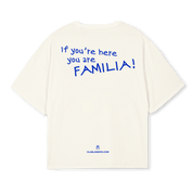 An off-white short-sleeve t-shirt shown from the back, featuring the blue text 'if you're here you are FAMILIA!' printed on the back, with 'CLUBLAJESITA.COM' printed near the bottom hem.